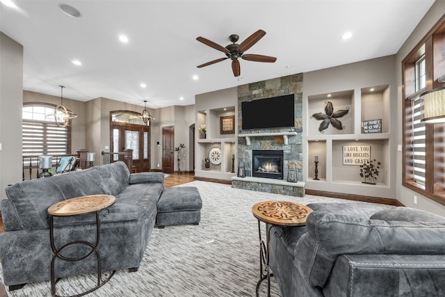 living room with recessed lighting, baseboards, built in shelves, a fireplace, and ceiling fan with notable chandelier