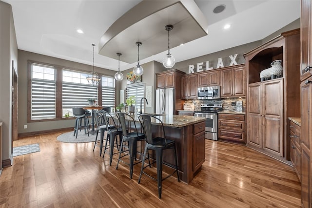 kitchen featuring a breakfast bar area, wood finished floors, appliances with stainless steel finishes, a tray ceiling, and an island with sink