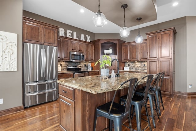 kitchen with tasteful backsplash, dark wood finished floors, appliances with stainless steel finishes, light stone countertops, and a sink