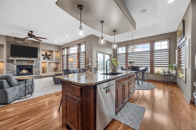 kitchen featuring a stone fireplace, a sink, built in features, stainless steel dishwasher, and light wood-type flooring