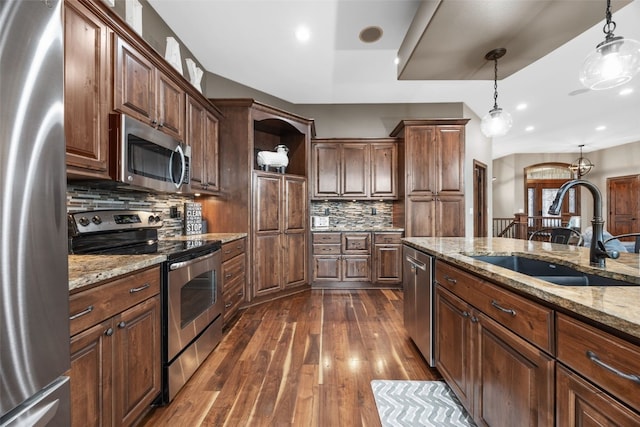 kitchen with light stone counters, a sink, appliances with stainless steel finishes, dark wood-style floors, and pendant lighting