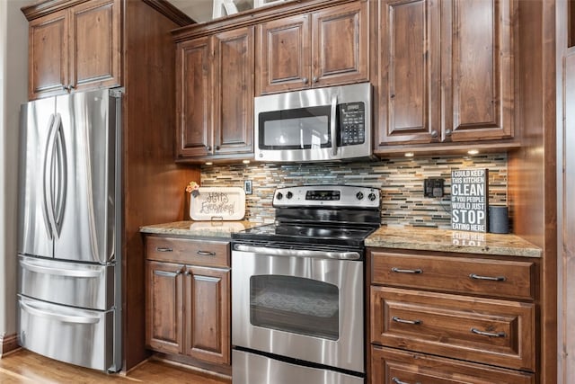 kitchen featuring light stone countertops, appliances with stainless steel finishes, decorative backsplash, and wood finished floors