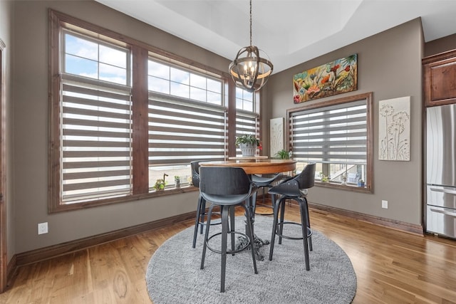 dining room with a notable chandelier, a tray ceiling, light wood-style flooring, and baseboards