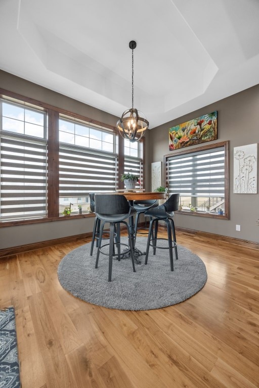 dining room with a raised ceiling, baseboards, an inviting chandelier, and wood finished floors