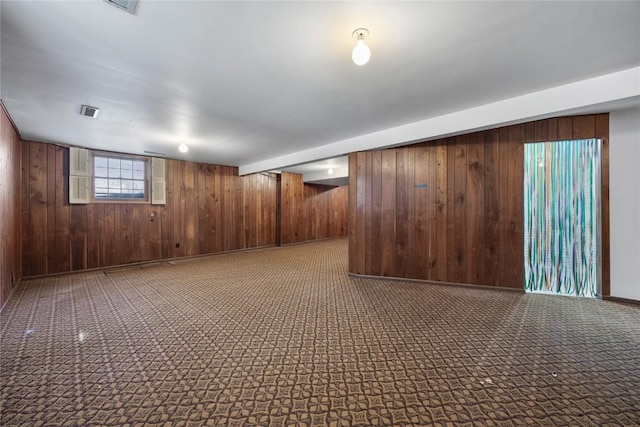 basement featuring carpet flooring, wood walls, visible vents, and baseboards