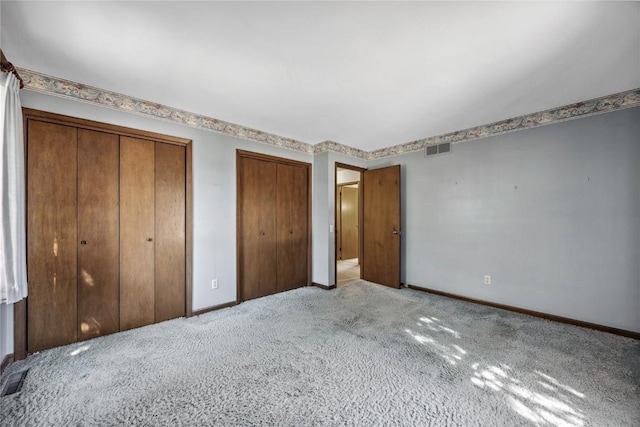 unfurnished bedroom with baseboards, carpet, visible vents, and multiple closets