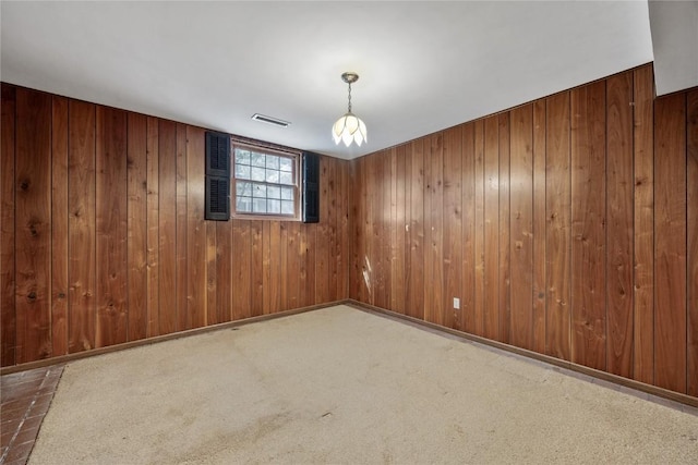 empty room with wood walls, carpet, visible vents, and baseboards