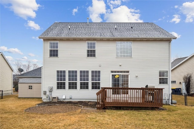 rear view of property with fence, a deck, a lawn, and roof with shingles