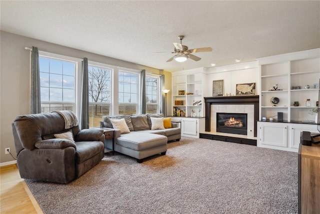 living room with a ceiling fan, a tile fireplace, built in features, and baseboards