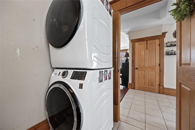 laundry area featuring light tile patterned floors, stacked washing maching and dryer, and baseboards