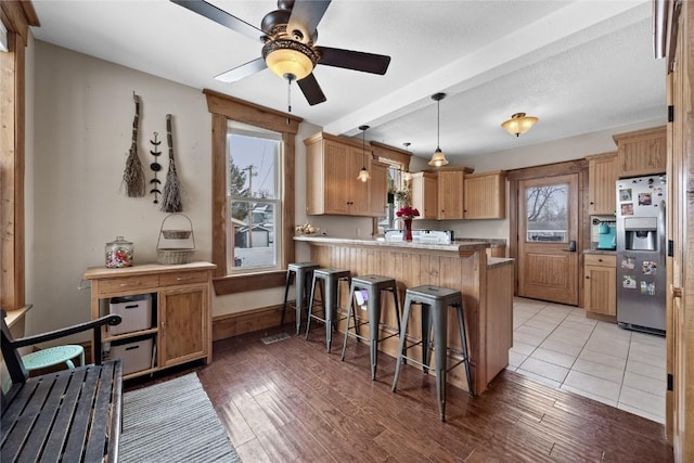 kitchen with stainless steel fridge with ice dispenser, light countertops, light wood-type flooring, a peninsula, and a kitchen bar