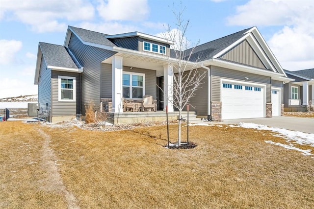 craftsman inspired home with concrete driveway, stone siding, an attached garage, covered porch, and central air condition unit