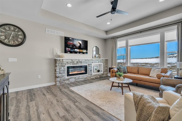 living area with a raised ceiling, visible vents, a fireplace, and baseboards