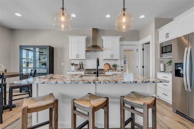 kitchen featuring a breakfast bar, white cabinets, appliances with stainless steel finishes, wall chimney exhaust hood, and tasteful backsplash