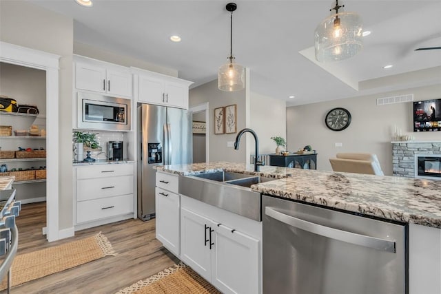 kitchen with light wood-style flooring, a fireplace, a sink, appliances with stainless steel finishes, and light stone countertops