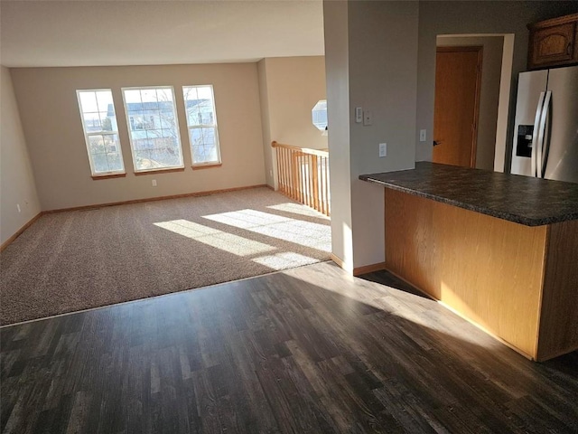 kitchen with stainless steel fridge, baseboards, dark countertops, wood finished floors, and a peninsula