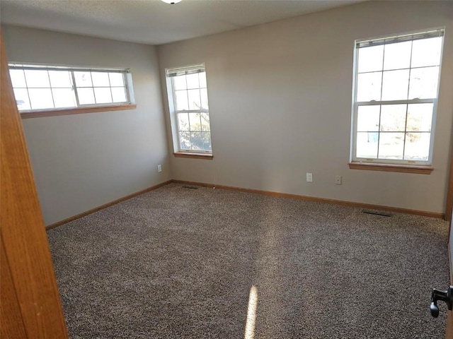 empty room featuring carpet, visible vents, and baseboards