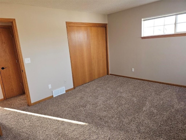 unfurnished bedroom featuring a textured ceiling, visible vents, baseboards, a closet, and carpet