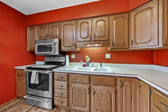 kitchen featuring light wood-style flooring, appliances with stainless steel finishes, light countertops, a textured ceiling, and a sink