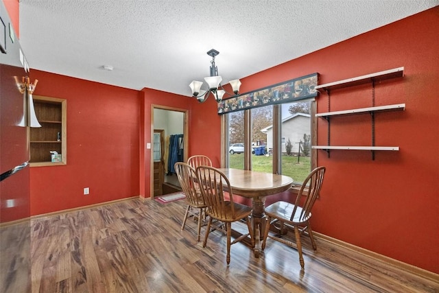 dining space with an inviting chandelier, a textured ceiling, baseboards, and wood finished floors