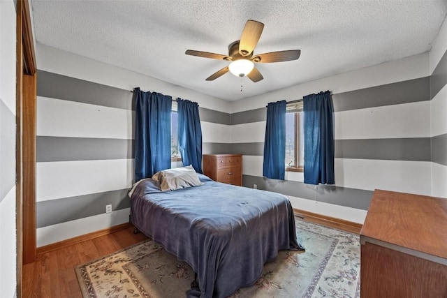 bedroom with a ceiling fan, a textured ceiling, baseboards, and wood finished floors