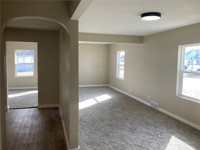 empty room featuring visible vents, arched walkways, and baseboards