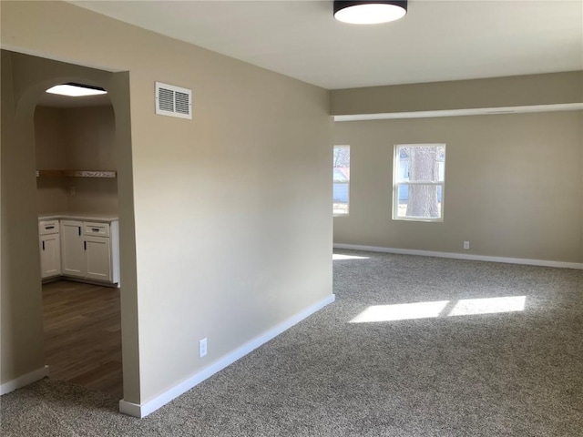 unfurnished room with arched walkways, dark carpet, visible vents, and baseboards