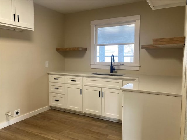 laundry room with cabinet space, light wood-style flooring, baseboards, and a sink