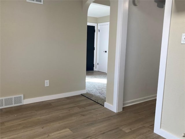 spare room with baseboards, visible vents, arched walkways, and wood finished floors