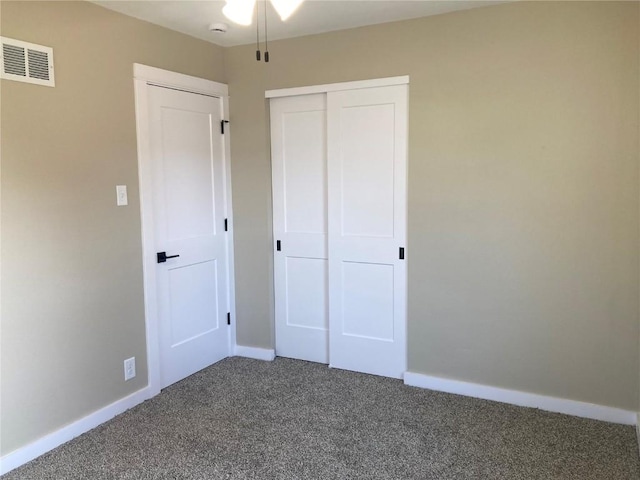 unfurnished bedroom featuring dark colored carpet, a closet, visible vents, and baseboards