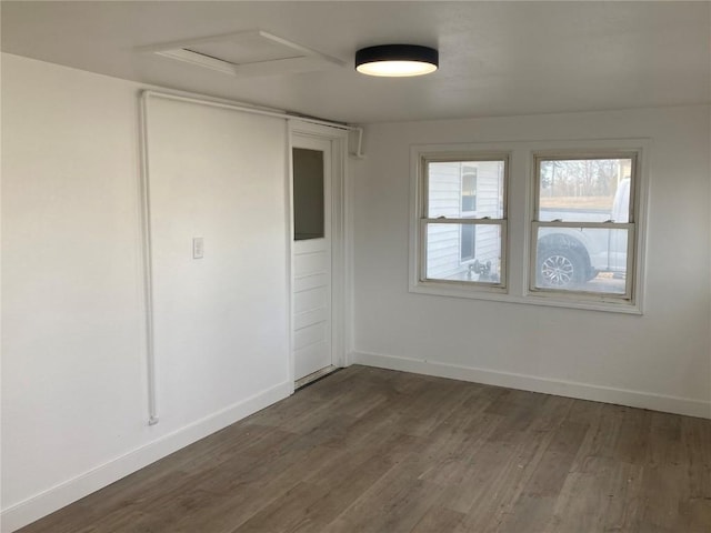 unfurnished room with dark wood-style floors, attic access, and baseboards