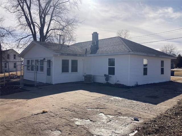 rear view of house featuring driveway, central AC unit, a patio, a chimney, and roof with shingles