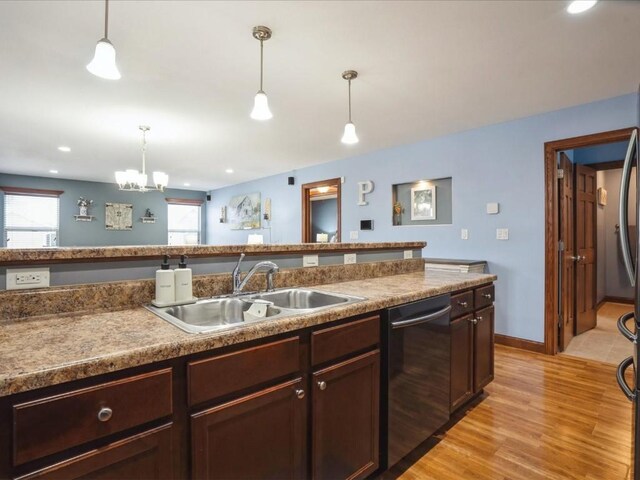 kitchen featuring hanging light fixtures, dishwashing machine, light wood-style floors, and a sink