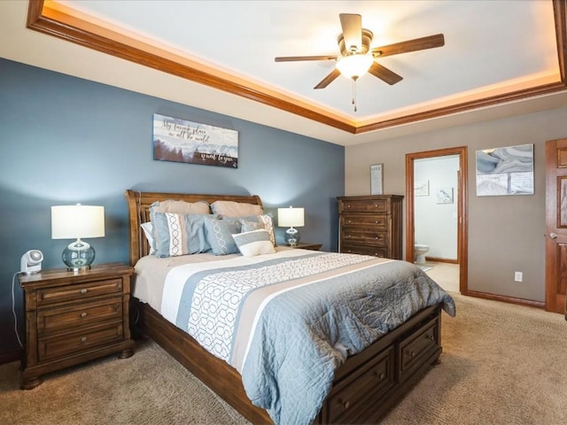 carpeted bedroom featuring a tray ceiling, baseboards, a ceiling fan, and ensuite bathroom