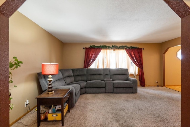 living area featuring arched walkways, a textured ceiling, carpet flooring, and baseboards