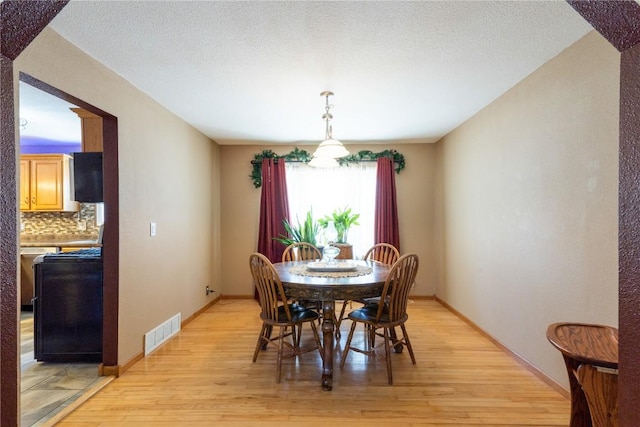 dining room with light wood-style floors, visible vents, a textured ceiling, and baseboards