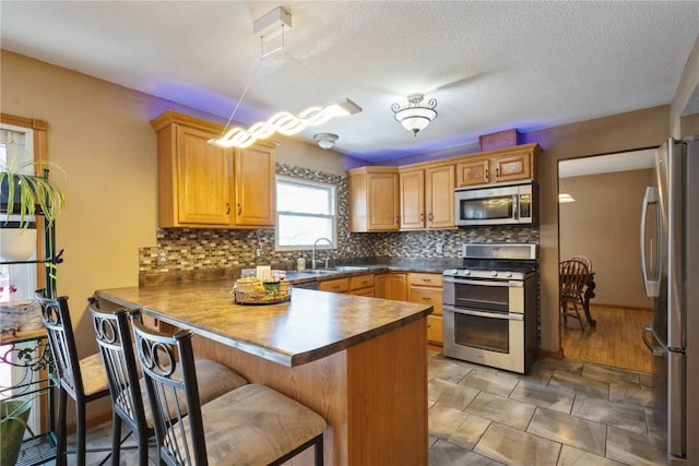 kitchen with decorative backsplash, dark countertops, a breakfast bar, a peninsula, and stainless steel appliances