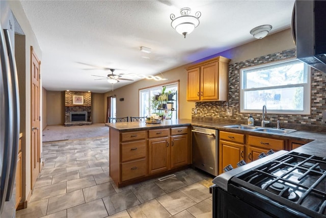 kitchen with stainless steel appliances, a peninsula, a fireplace, a sink, and dark countertops