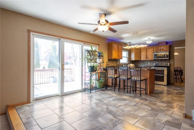 kitchen featuring tasteful backsplash, brown cabinetry, a breakfast bar area, a peninsula, and stainless steel appliances