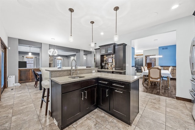 kitchen featuring an island with sink, a sink, a breakfast bar area, light tile patterned floors, and light stone countertops