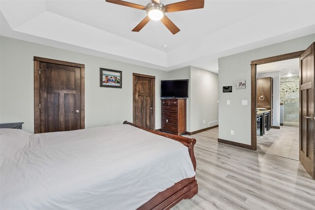 bedroom with a ceiling fan, visible vents, baseboards, a tray ceiling, and light wood-style flooring