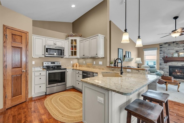 kitchen featuring light stone countertops, a peninsula, a sink, vaulted ceiling, and appliances with stainless steel finishes