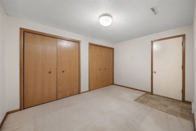 unfurnished bedroom with visible vents, two closets, baseboards, carpet floors, and a textured ceiling