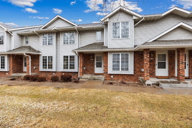 multi unit property with brick siding, a front yard, and roof with shingles