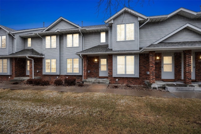 view of property featuring brick siding and roof with shingles