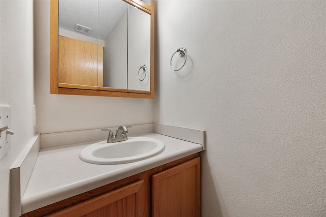 bathroom with vanity, a textured wall, visible vents, and a textured ceiling