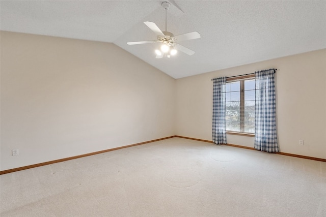 spare room featuring vaulted ceiling, carpet flooring, baseboards, and a textured ceiling