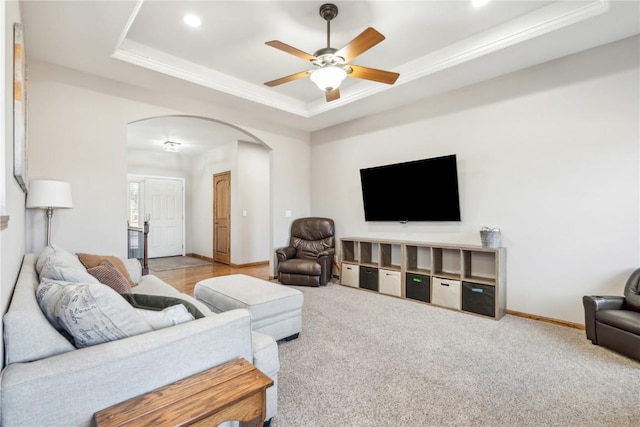 living room featuring baseboards, carpet, a tray ceiling, arched walkways, and a ceiling fan