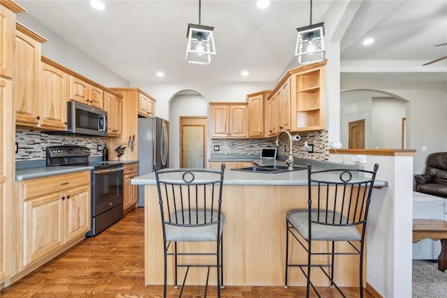 kitchen with light brown cabinets, a peninsula, arched walkways, a sink, and appliances with stainless steel finishes