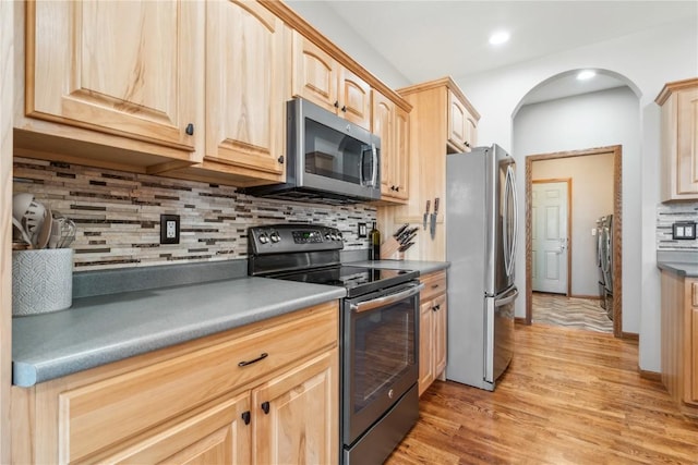 kitchen with independent washer and dryer, light brown cabinetry, backsplash, appliances with stainless steel finishes, and light wood finished floors